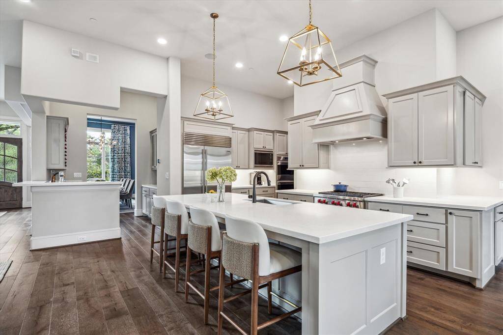 This designer kitchen showcases a refined palette of soft gray cabinetry, professional-grade appliances, and a waterfall-edge island that blends timeless elegance with modern functionality.