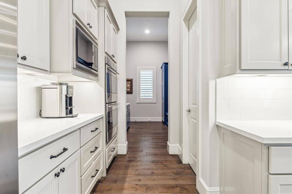 This well-appointed prep corridor offers additional counter space, double ovens, and abundant cabinetry—seamlessly connecting the kitchen to the mudroom and enhancing both function and flow.