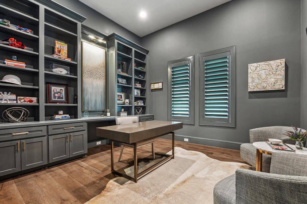 This richly appointed home office exudes sophistication with its dramatic wall color, custom built-in cabinetry, and designer lighting that highlights an art niche centerpiece. Dual shuttered windows and sleek furnishings complete the space, offering both style and focus for inspired productivity.