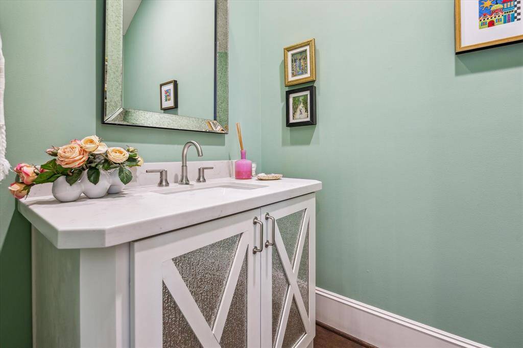 This charming powder bath delights with its soft green walls, elegant marble-topped vanity, and custom cabinetry featuring textured glass insets for a refined touch of personality.