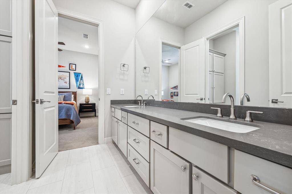 This well-designed secondary bathroom features a sleek double vanity with quartz countertops, modern fixtures, and ample storage, offering a stylish and functional space conveniently shared between two bedrooms.