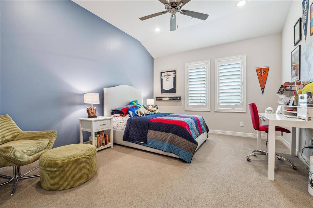 This cheerful secondary bedroom features soft carpet, a dramatic vaulted ceiling, and ample natural light from twin shuttered windows—offering a comfortable and versatile space perfect for rest, study, or play.