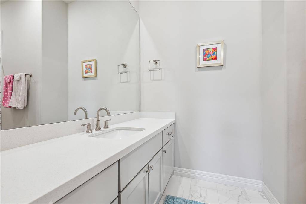 This stylish secondary bathroom features crisp white quartz countertops, soft gray cabinetry, and a sleek undermount sink, all accented by a full-height mirror and polished chrome fixtures for a clean, modern finish.
