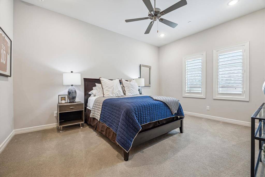 This spacious secondary bedroom offers a peaceful retreat with soft neutral tones, plush carpeting, and abundant natural light filtered through classic plantation shutters. A ceiling fan and recessed lighting add comfort and function, while the layout provides plenty of space for a large bed and additional furnishings.