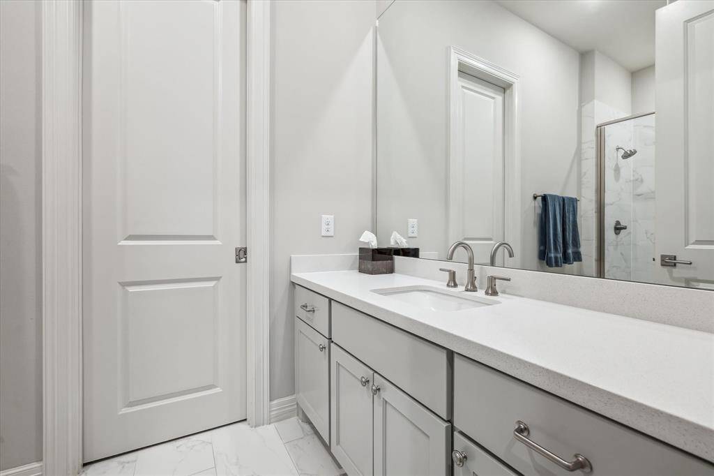 This secondary bathroom features a spacious quartz-topped vanity, sleek undermount sink, and a frameless glass shower with elegant tile surround—offering both function and style in a polished, neutral palette.