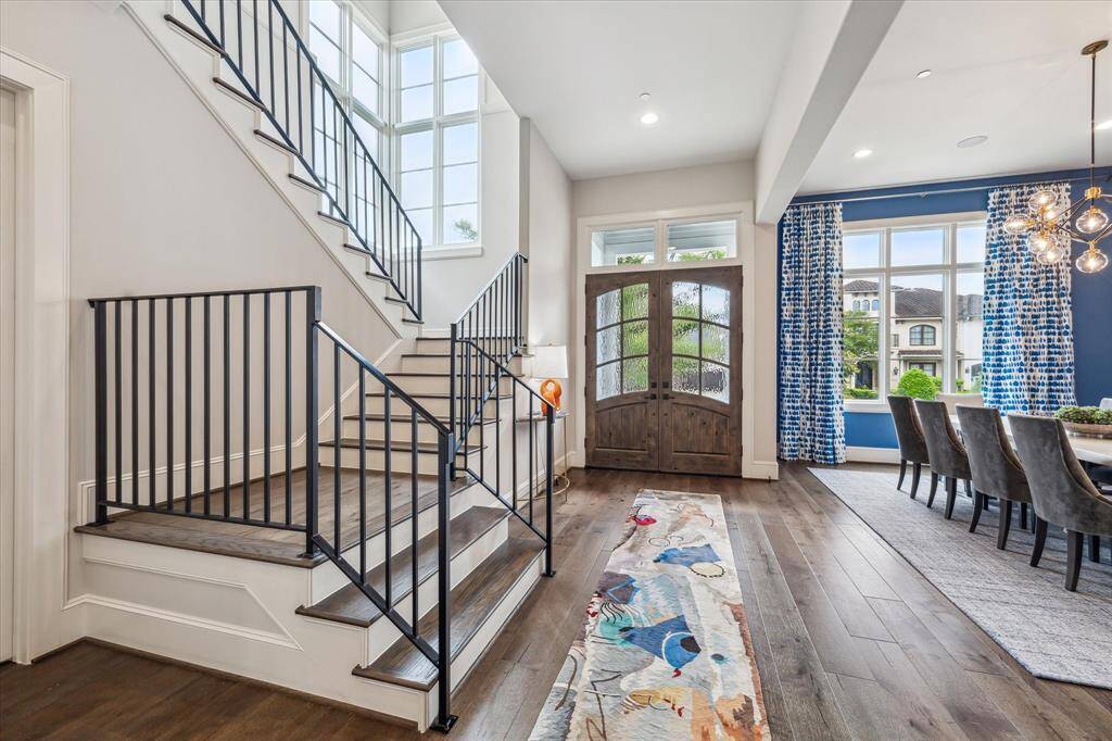 The grand entry makes a striking first impression with soaring ceilings, a dramatic wall of windows, and richly stained double doors that open to elegant hardwood floors and a sophisticated open layout.