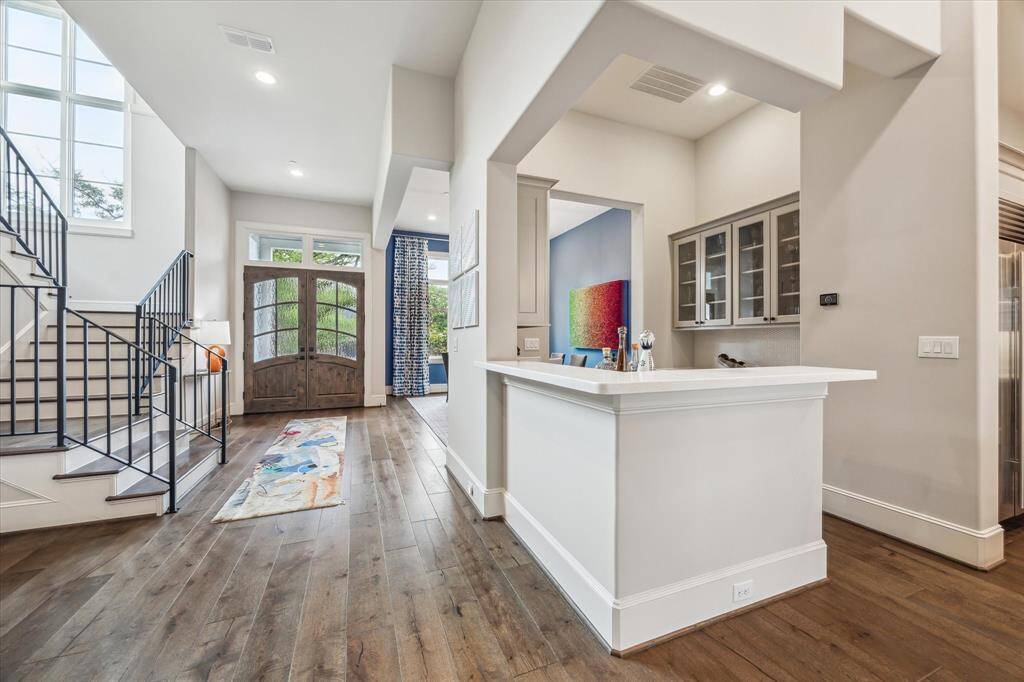 An additional view of the entry reveals the home's airy, open-concept design, where wide-plank hardwood floors flow seamlessly past the dramatic staircase, custom wet bar, and formal dining room