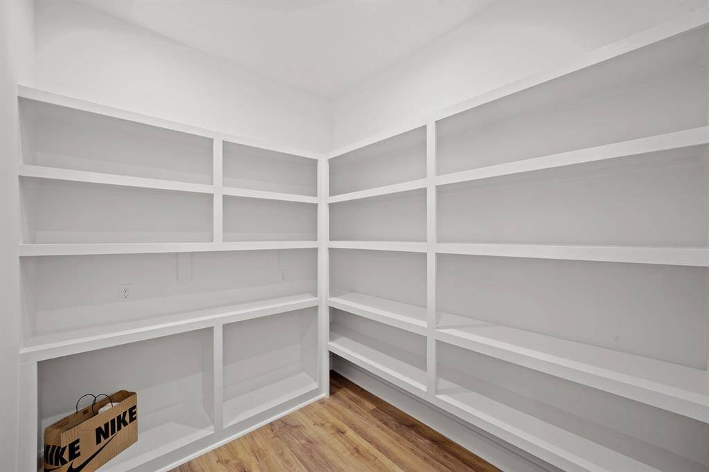 Spacious walk-in pantry with white built-in shelves and wood flooring, ideal for organized storage.