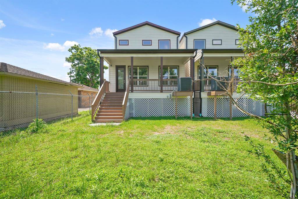 This photo showcases a charming two-story home with a raised porch and steps leading to a grassy backyard. The exterior features light siding with brown trim, and there's a lattice detail below the porch. The property is adjacent to a fenced area, providing a sense of privacy.