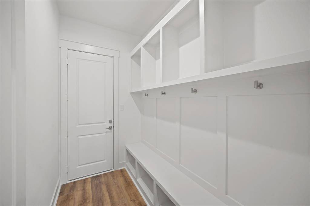 This is a bright, modern mudroom featuring white cabinetry with open cubbies, wall hooks, and a built-in bench. The space is accented by light wood flooring and a clean, minimalist design.