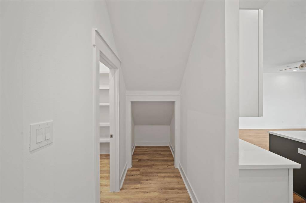 This photo shows a bright, narrow hallway with wood flooring. It leads to a small storage area and possibly connects to a room with visible shelving. The space has a modern and clean design.