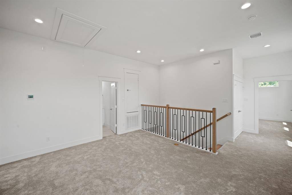This photo shows a bright, open Game Room with neutral carpeting, recessed lighting, and a modern staircase with a wooden handrail and black metal spindles. The space connects to multiple rooms, offering a versatile layout.