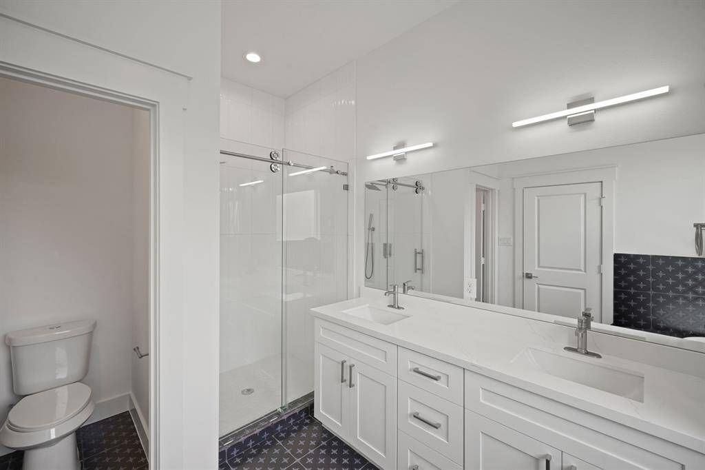 This modern bathroom features a spacious double vanity with sleek fixtures, a large mirror, contemporary lighting, a glass-enclosed shower, and stylish tiled flooring.