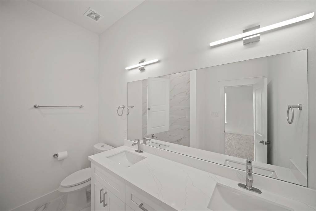 Modern bathroom with a sleek double vanity, large mirror, and bright lighting. Features a minimalist design with neutral colors and a clean aesthetic.