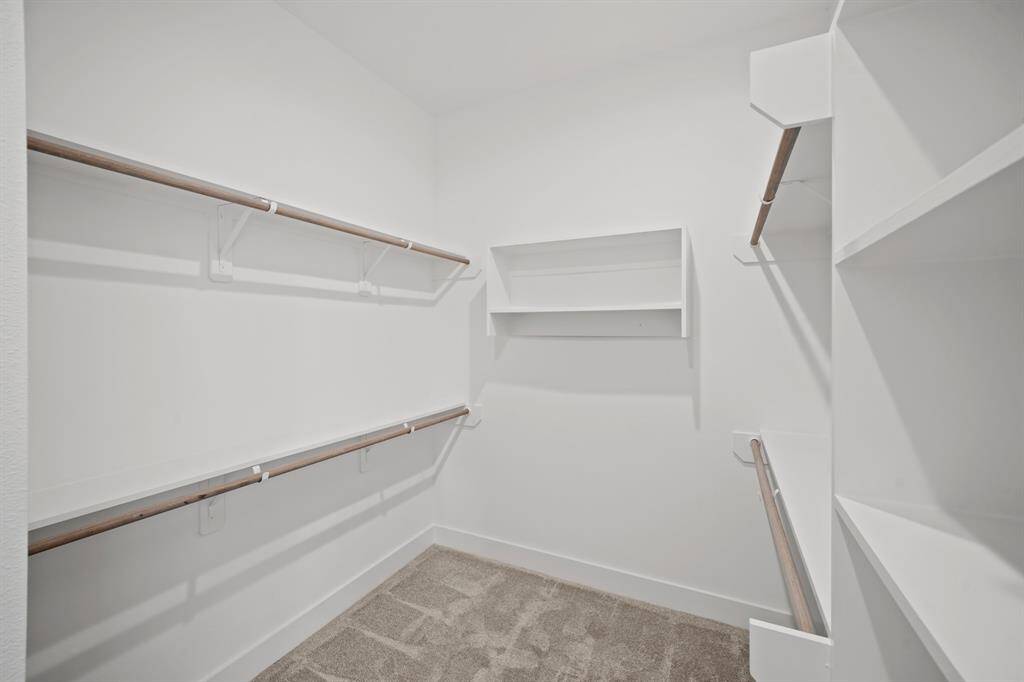 This is a spacious walk-in closet with multiple shelves and hanging rods, offering ample storage space. The neutral color scheme and carpeted flooring create a clean and inviting atmosphere.