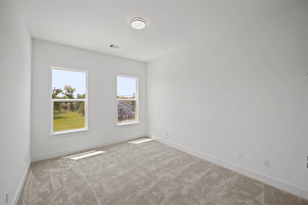 Bright, spacious bedroom with neutral carpeting, two large windows offering plenty of natural light, and a clean, minimalist design.