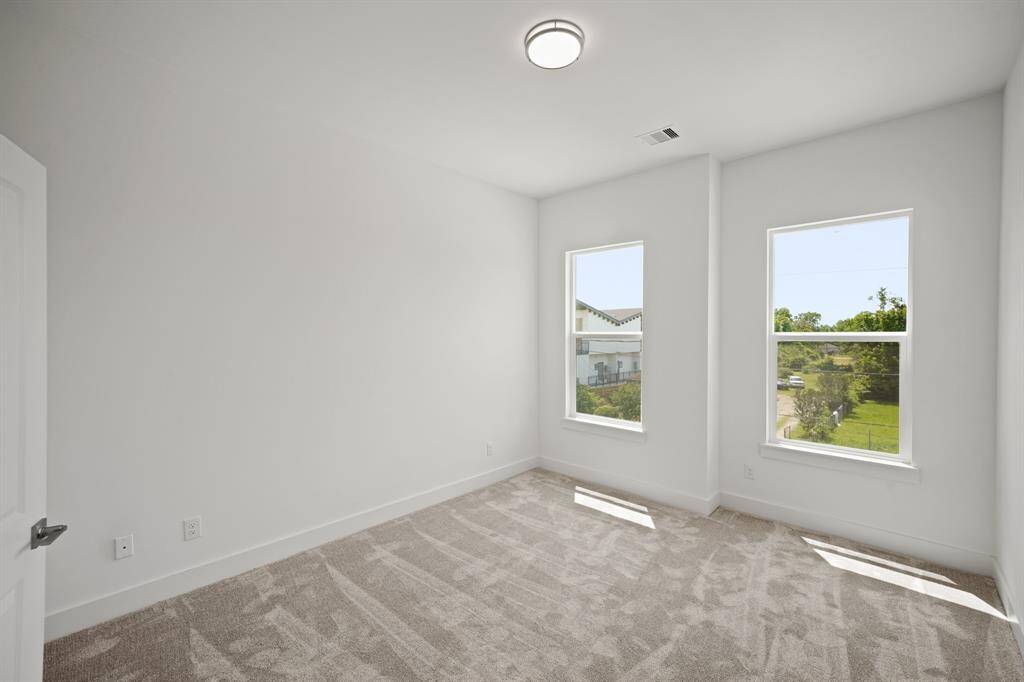 This is a bright, empty room with neutral walls and new carpeting. It features two large windows, allowing plenty of natural light and a view of greenery outside. Ideal for a bedroom or office space.