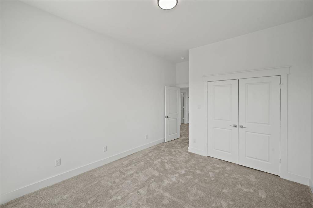 This photo shows a bright, spacious room with neutral walls and carpeted flooring. It features a double-door closet and a ceiling light, offering ample storage and a clean, modern look.