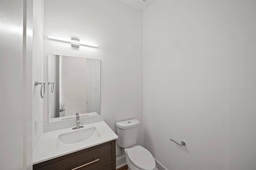 This is a modern, compact bathroom with a sleek vanity and sink, a wall-mounted mirror, and a toilet. It features minimalistic design with bright lighting and neutral tones.