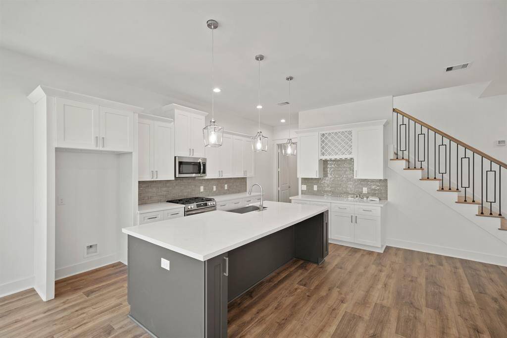 This photo showcases a modern kitchen with a large island, pendant lighting, and ample white cabinetry. The space features a stylish backsplash, stainless steel appliances, and hardwood floors. A staircase with contemporary railing is visible, adding elegance to the open-plan layout.