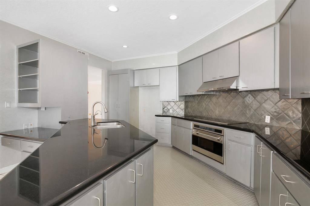 This is a modern kitchen with stainless steel appliances, sleek gray cabinetry, and dark countertops. It features a tiled backsplash and ample storage space.