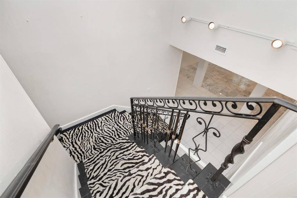 Elegant interior staircase featuring a bold zebra-patterned carpet, ornate black metal railing, and modern lighting fixtures, leading down to a spacious area with marble flooring.