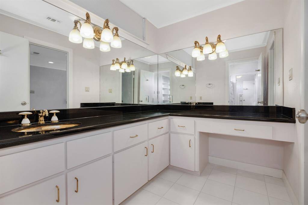 This is a spacious bathroom featuring a large vanity with ample cabinetry, elegant gold fixtures, and a wide mirror.