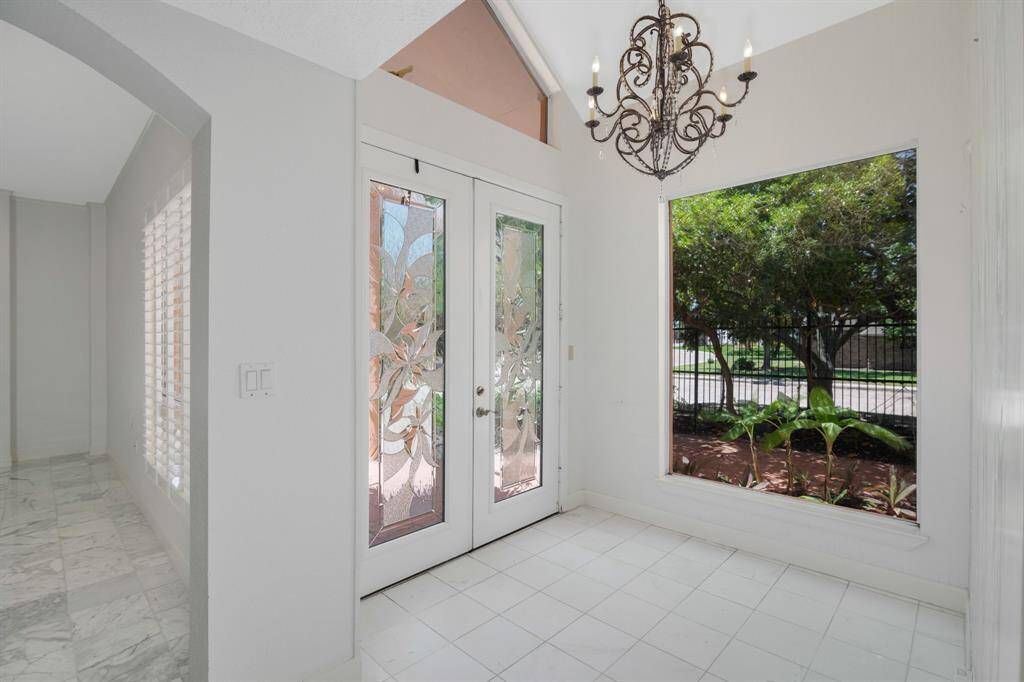 This is a bright, airy room with marble flooring and large French doors leading to a view of lush greenery outside. An elegant chandelier adds a touch of sophistication.