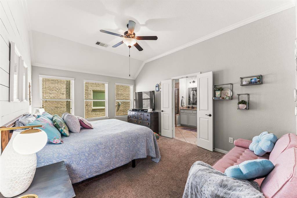 The bright and spacious primary bedroom features a vaulted ceiling with a ceiling fan, large windows for natural light, and an en-suite bathroom. The room is tastefully decorated with neutral tones, creating a welcoming atmosphere.