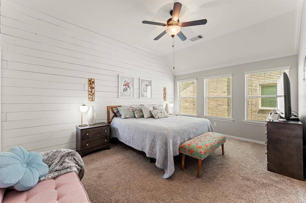 The primary bedroom is spacious and inviting, featuring a cozy atmosphere with neutral, plush carpet, and a stylish shiplap accent wall. Natural light floods in through three windows, enhancing the room's warmth.