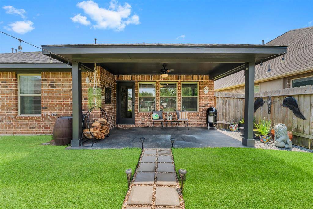 Charming backyard with a covered patio featuring a ceiling fan, seating area, and space for a grill. There is a gas plumb for your grill or future outdoor kitchen! The well-maintained lawn and decorative accents create a welcoming outdoor retreat.