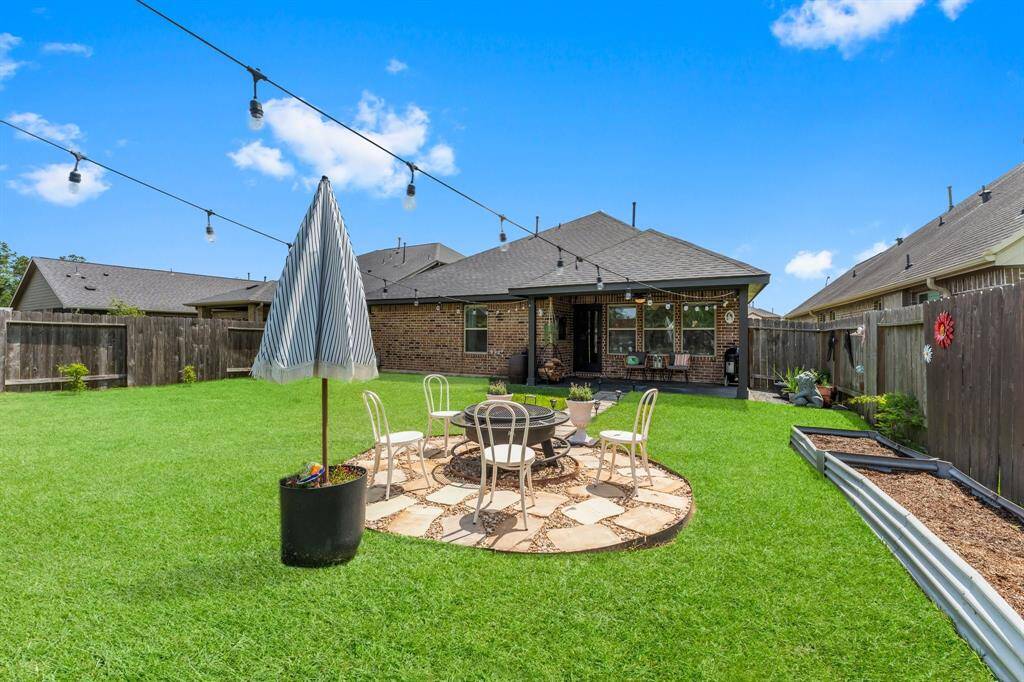 Spacious backyard with well-maintained lawn, patio area for seating, string lights, and garden beds. Perfect for outdoor gatherings and relaxation.