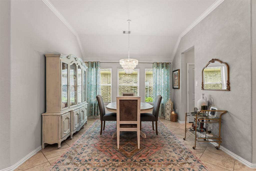 The dining room features elegant tile flooring and a large window with sheer curtains, providing natural light. It includes a stylish chandelier, and crown molding creating a cozy and inviting atmosphere.