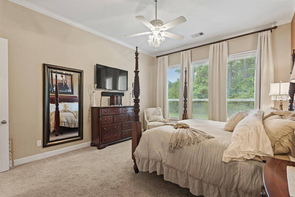 Unwind after a long day in spacious primary bedroom! Featuring lots of natural light, carpet floors, privacy blinds, crown molding details, and a ceiling fan.
