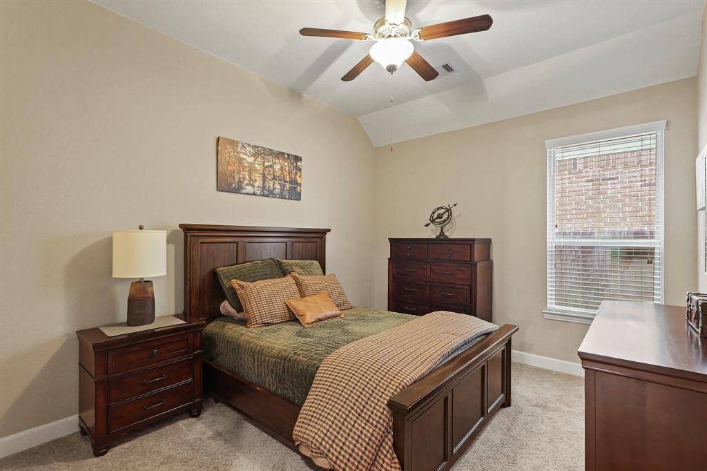 Virtually Staged: This secondary bedroom in the first floor has carpet floors, a window with privacy blinds, and a tray ceiling with a ceiling fan.