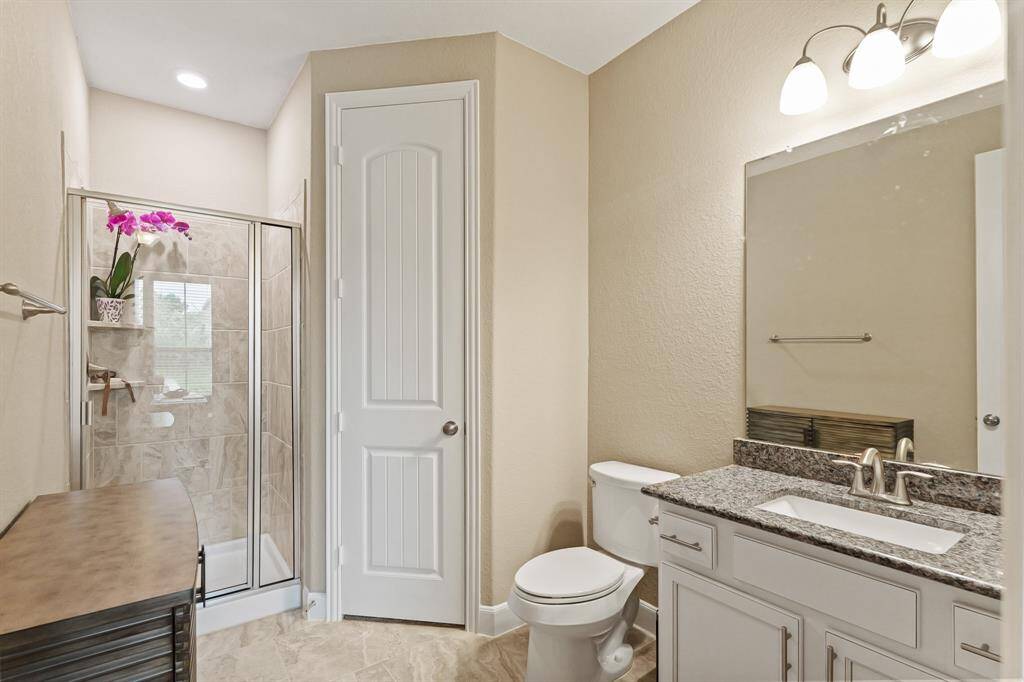 This secondary bathroom has tile floors, a walk-in shower, granite countertops and backsplash, and a walk-in closet.