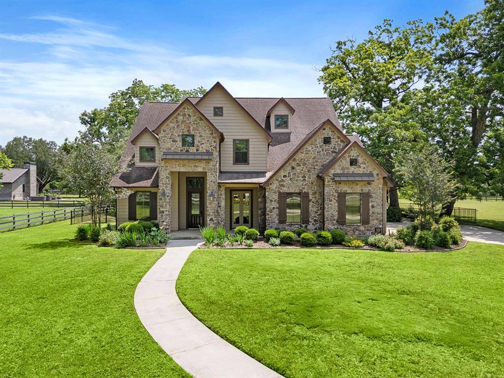 This charming home features a stone facade with a welcoming front entrance and beautifully landscaped front yard. It is situated in a serene, spacious setting with lush green lawns and mature trees, offering a peaceful and private atmosphere.