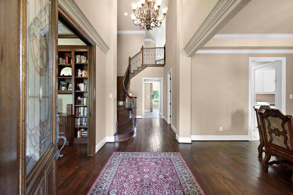 This entryway features rich hardwood floors, a grand staircase with elegant iron balusters, and a beautiful chandelier.