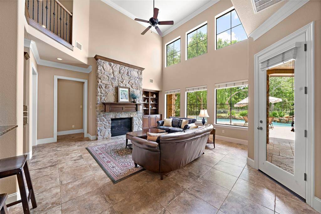 This spacious living room with stone fireplace opens to a patio with a view of the pool, creating a seamless indoor-outdoor living experience.