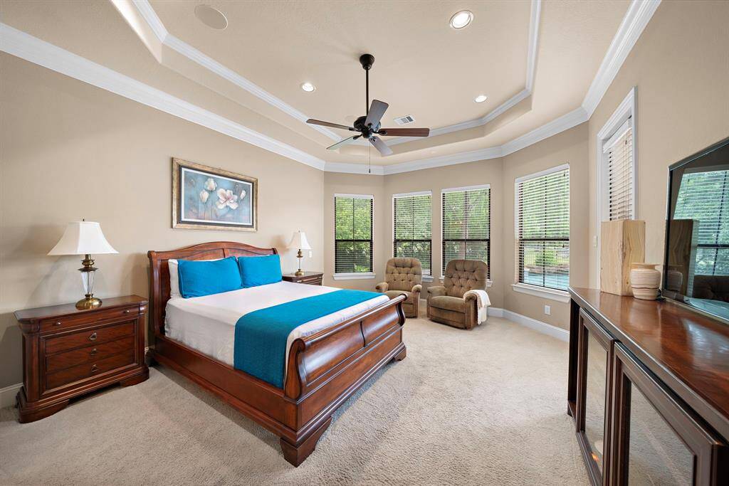 Luxurious primary suite featuring bay windows, a coffered ceiling, ceiling fan, and direct patio access.