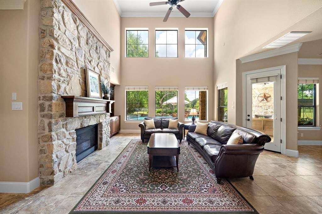This spacious living room features a stunning stone fireplace, high ceilings, and large windows that flood the space with natural light as well as offer the most picturesque views of the back patio.