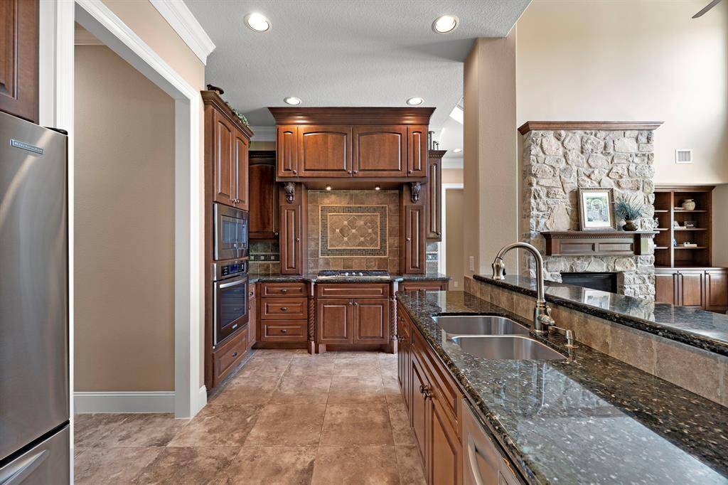 This kitchen features elegant dark wood cabinetry, granite countertops, and modern stainless-steel appliances. It includes a stylish tile backsplash, gas cooktop, and large walk-in pantry.