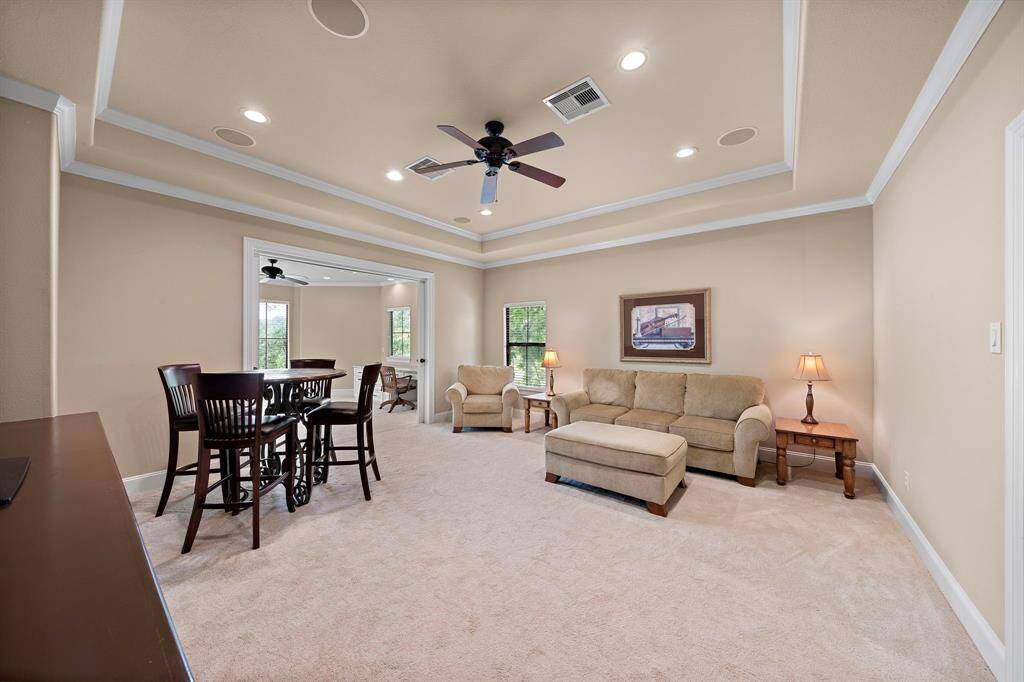 This spacious upstairs living area/gameroom features neutral walls and carpeting, creating a warm and inviting atmosphere. This space is large enough to comfortably fit a cozy seating arrangement with a sofa and ottoman and a high-top dining table set. Ceiling fans and large windows enhance comfort and natural light.