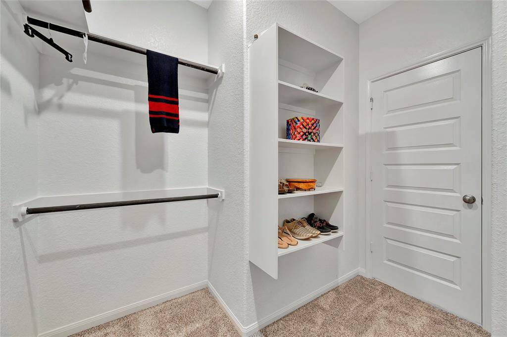 his spacious walk-in closet is a dream for organization and style, featuring dedicated shelving for shoes and hanging rods to keep your clothing neatly arranged. The custom shelving offers ample space to neatly display your shoe collection, while the hanging rods provide plenty of room for clothing, ensuring everything has its place