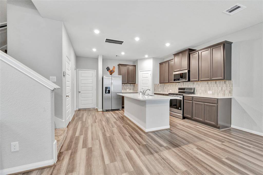 View from living area.  The kitchen is anchored by light-colored countertops, made of durable quartz or marble, offering a bright, airy feel that contrasts beautifully with the darker cabinetry. The countertops' subtle veining enhances the modern appeal, making it both practical for daily use and visually pleasing.