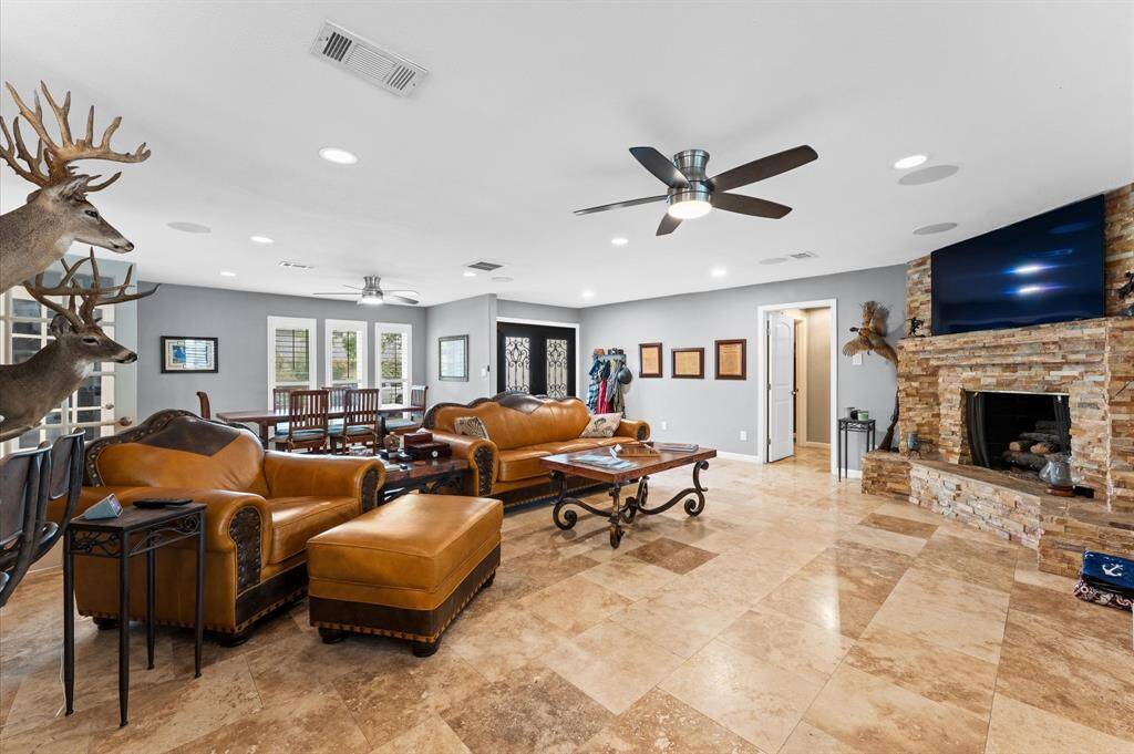 The open living room features a stone fireplace with cozy seating, and a ceiling fan. It boasts large windows with shutters, offering plenty of natural light. The open layout flows seamlessly and it is ideal for entertaining.