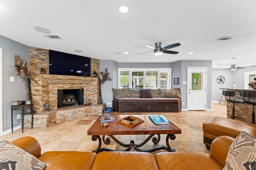 Spacious living area with a cozy stone fireplace and elegant tile flooring. Features leather seating, rustic décor, and an open layout. Natural light floods through large windows, creating a warm, inviting atmosphere.