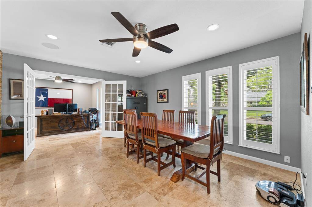 This cozy dining area features a modern ceiling fan, neutral grey walls, and a round table with bar stools. Natural light fills the space through a window with shutters, creating a bright and inviting atmosphere.