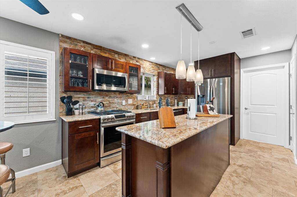 Modern kitchen with stainless steel appliances, granite countertops, and rich wooden cabinetry. Features a stone backsplash, pendant lighting, and a spacious layout for cooking and entertaining.