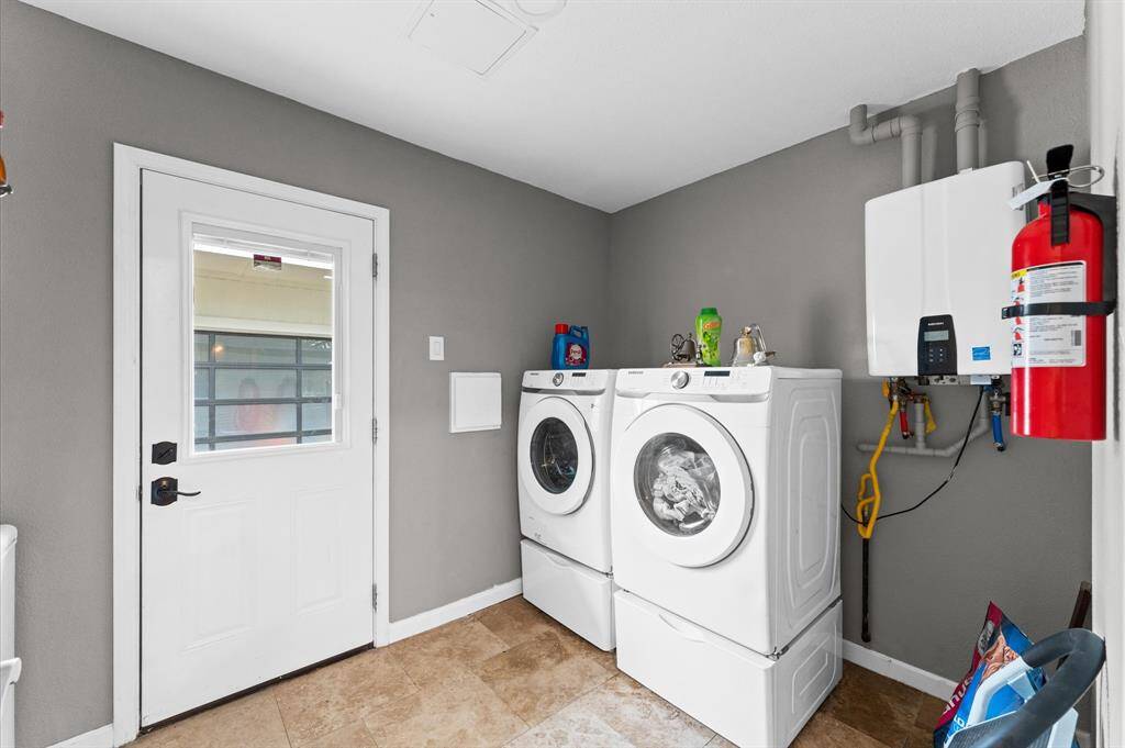 Well-organized laundry room with washer and dryer set against a neutral wall. The space includes a utility sink, tankless water heater, and a side door for easy access. The room is bright and functional, perfect for household chores.
